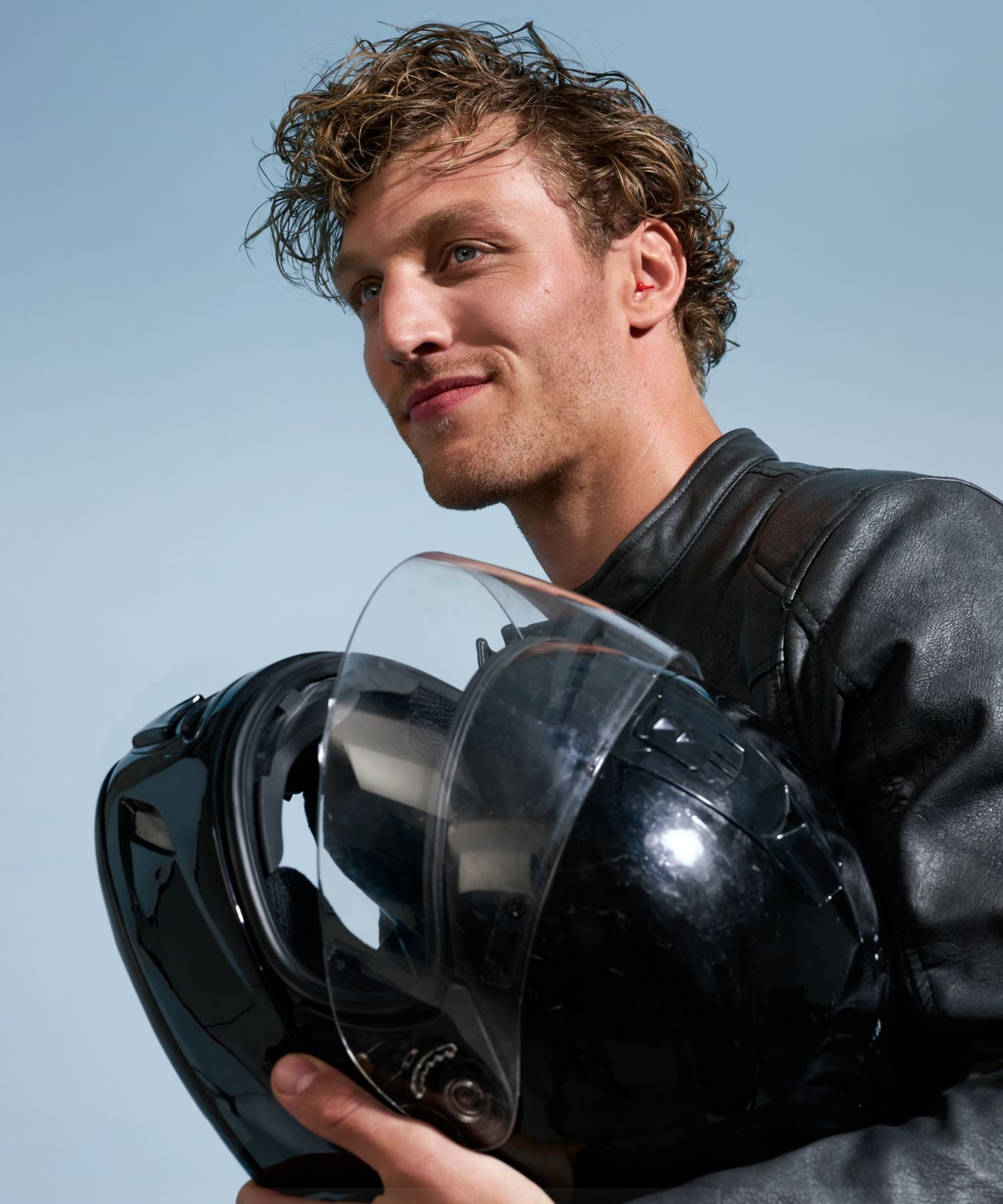 A man holding a motorcycle helmet wearing Alpine MotoSafe earplugs.