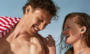 A woman and a man at the beach wearing Alpine Watersafe Pro earplugs.