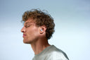 Left side of a man, with curly hair, eyes closed and calm facial expression, with Alpine Silence blue in his ear