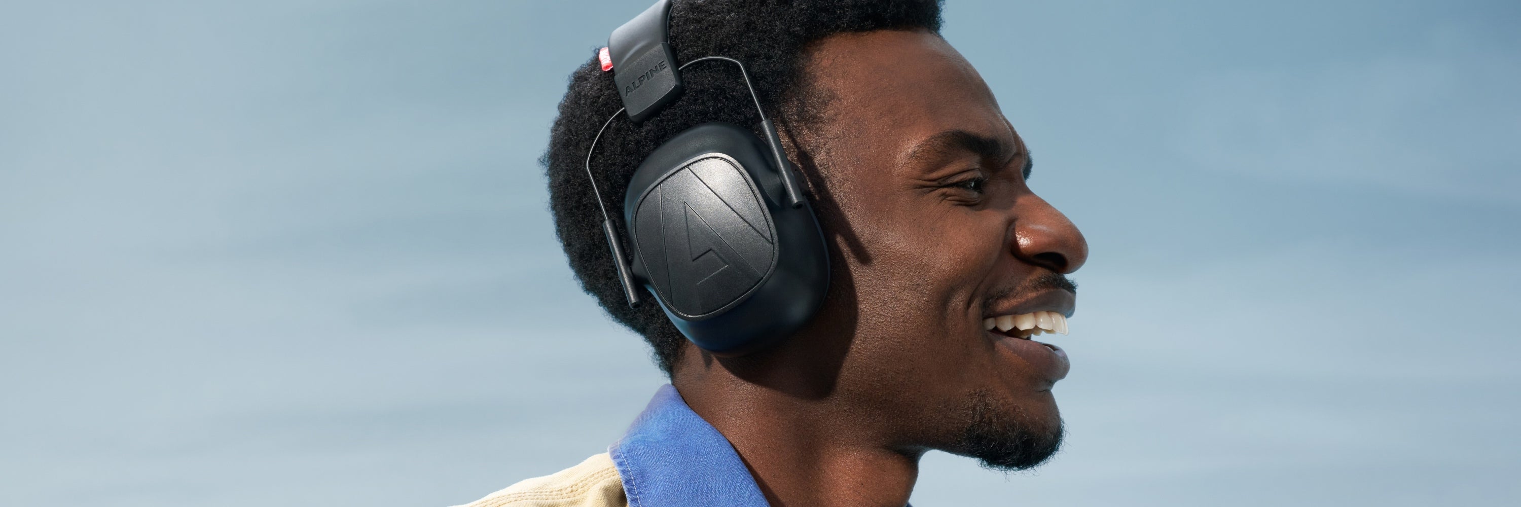 Man wearing over-ear headphones against a clear blue sky