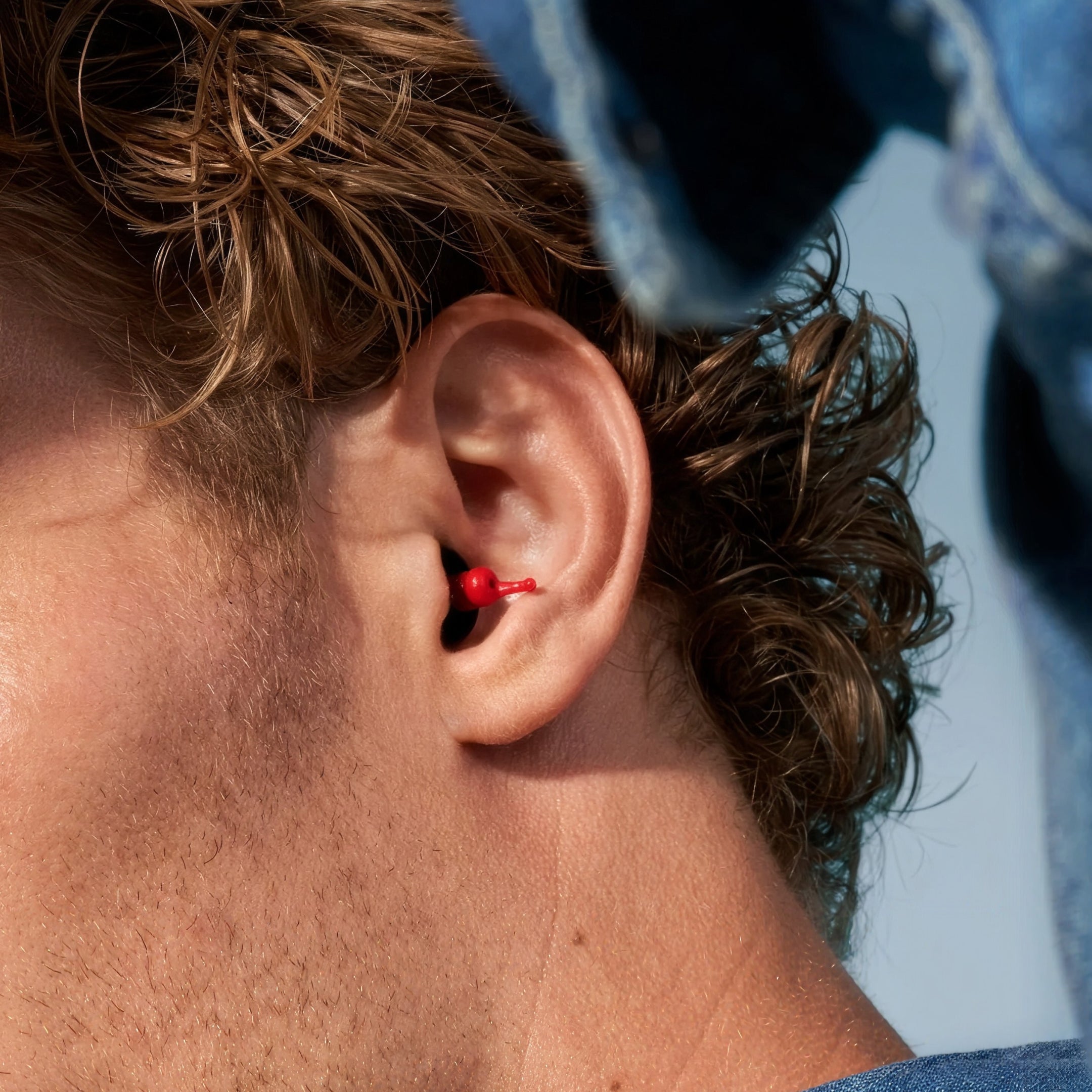 Alpine MotoGP™ earplug worn in the ear by a man with curly hair in a denim jacket 